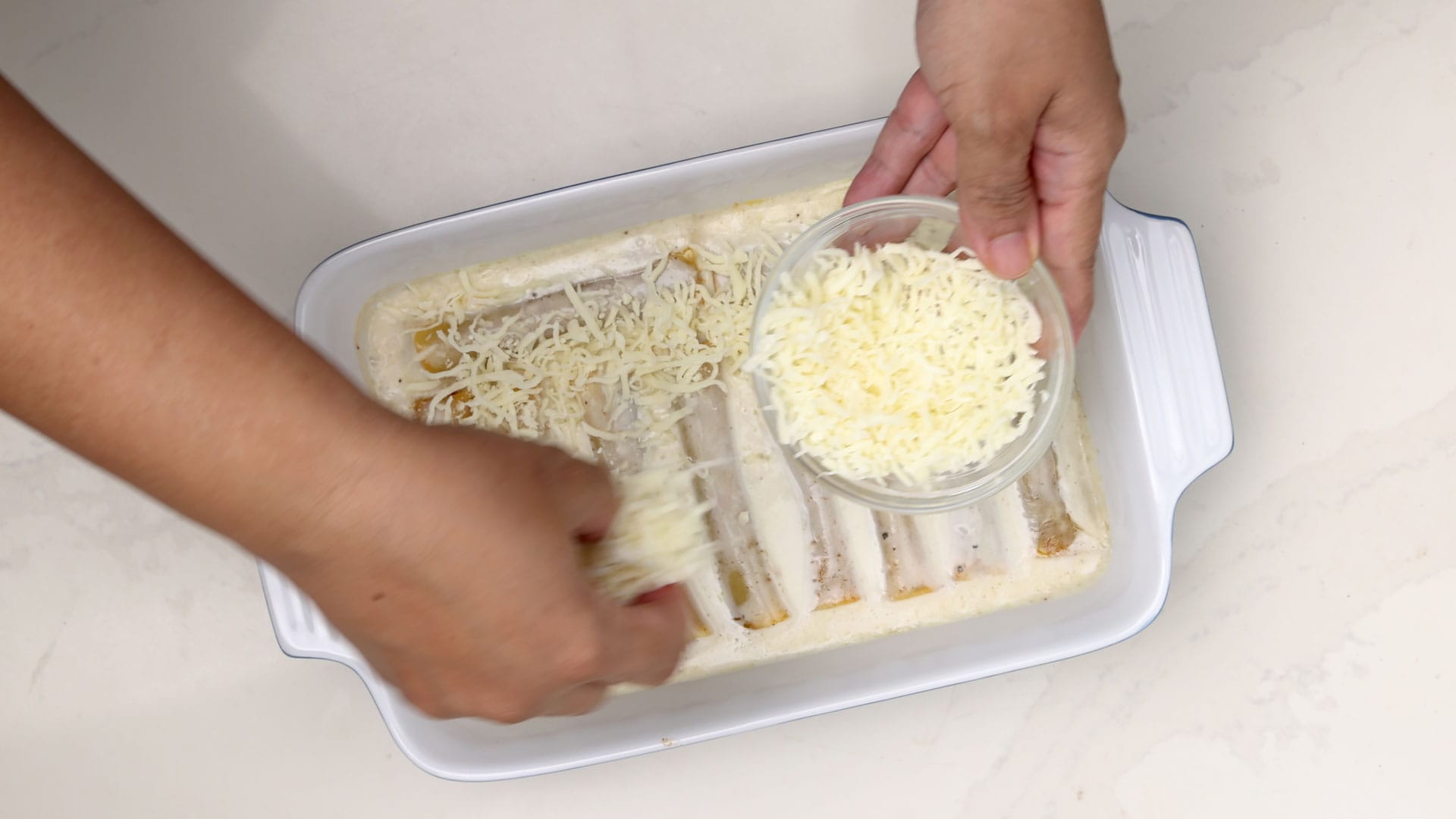 Covering cannelloni with cheese.