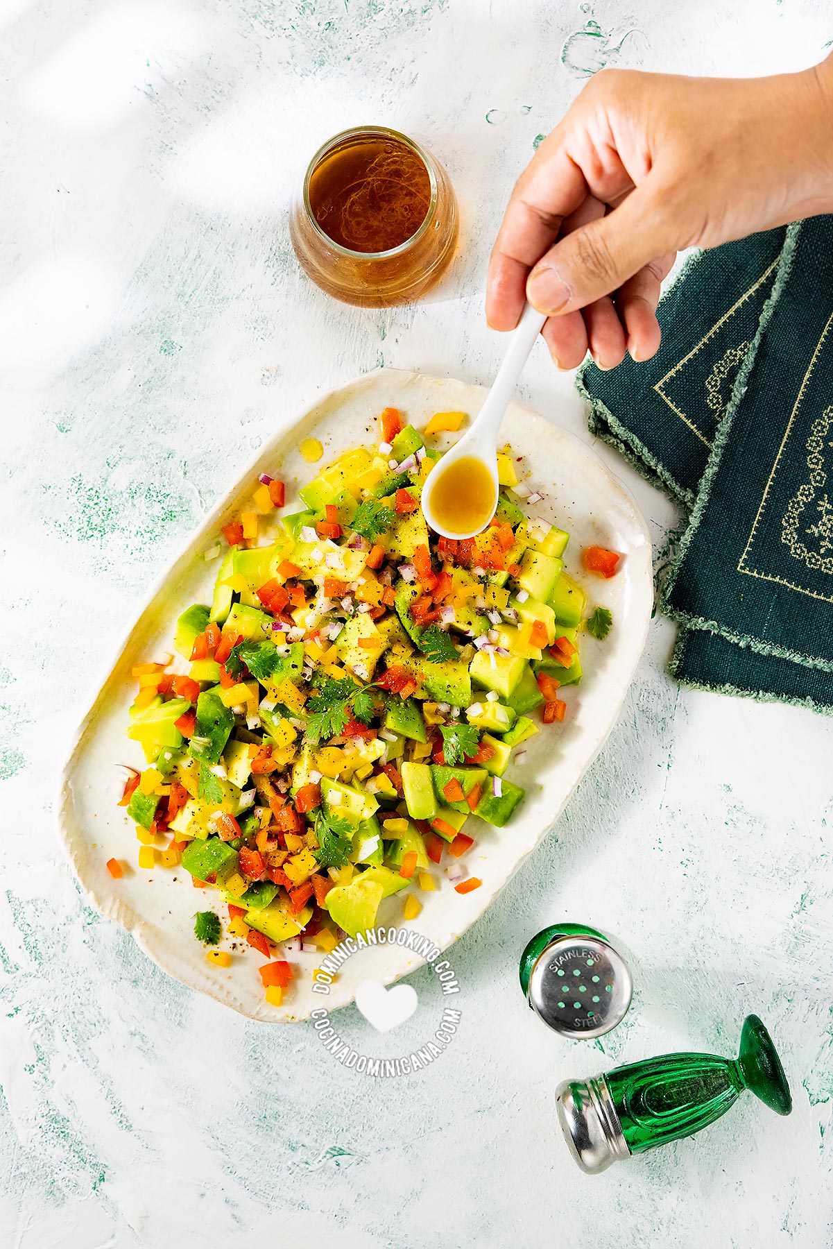 Hand pouring vinaigrette on ensalada de aguacate (avocado salad).